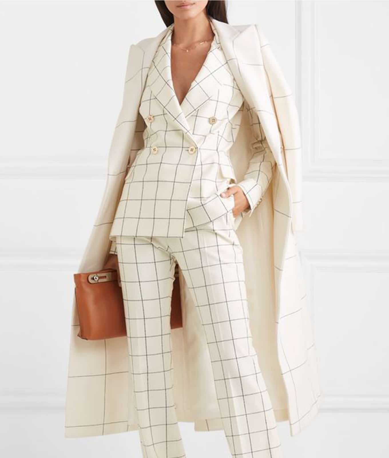 Women wearing white suit and long smart coat with a tan leather handbag.
